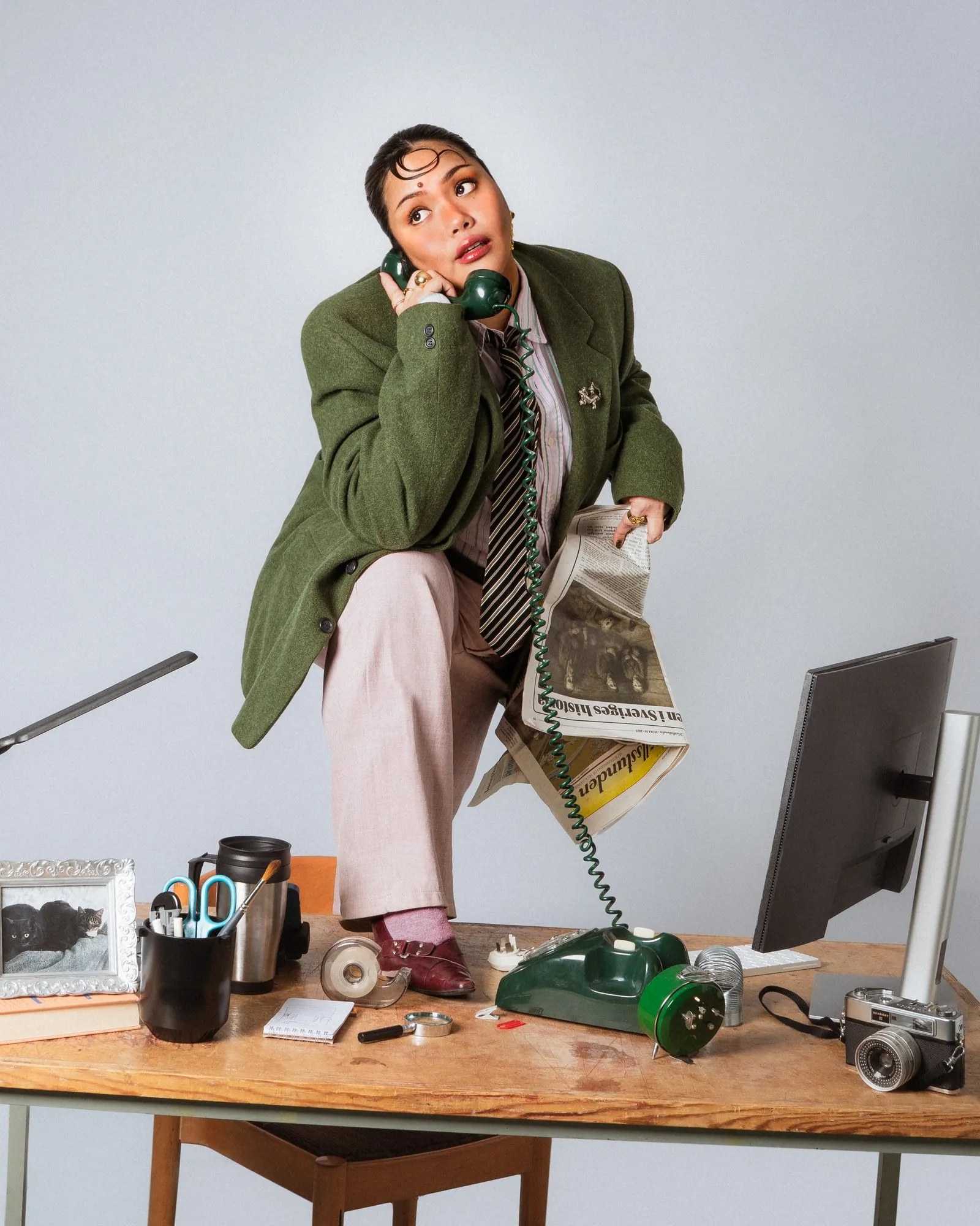 Thurees kneeling on a desk with a newspaper and a green rotary phone