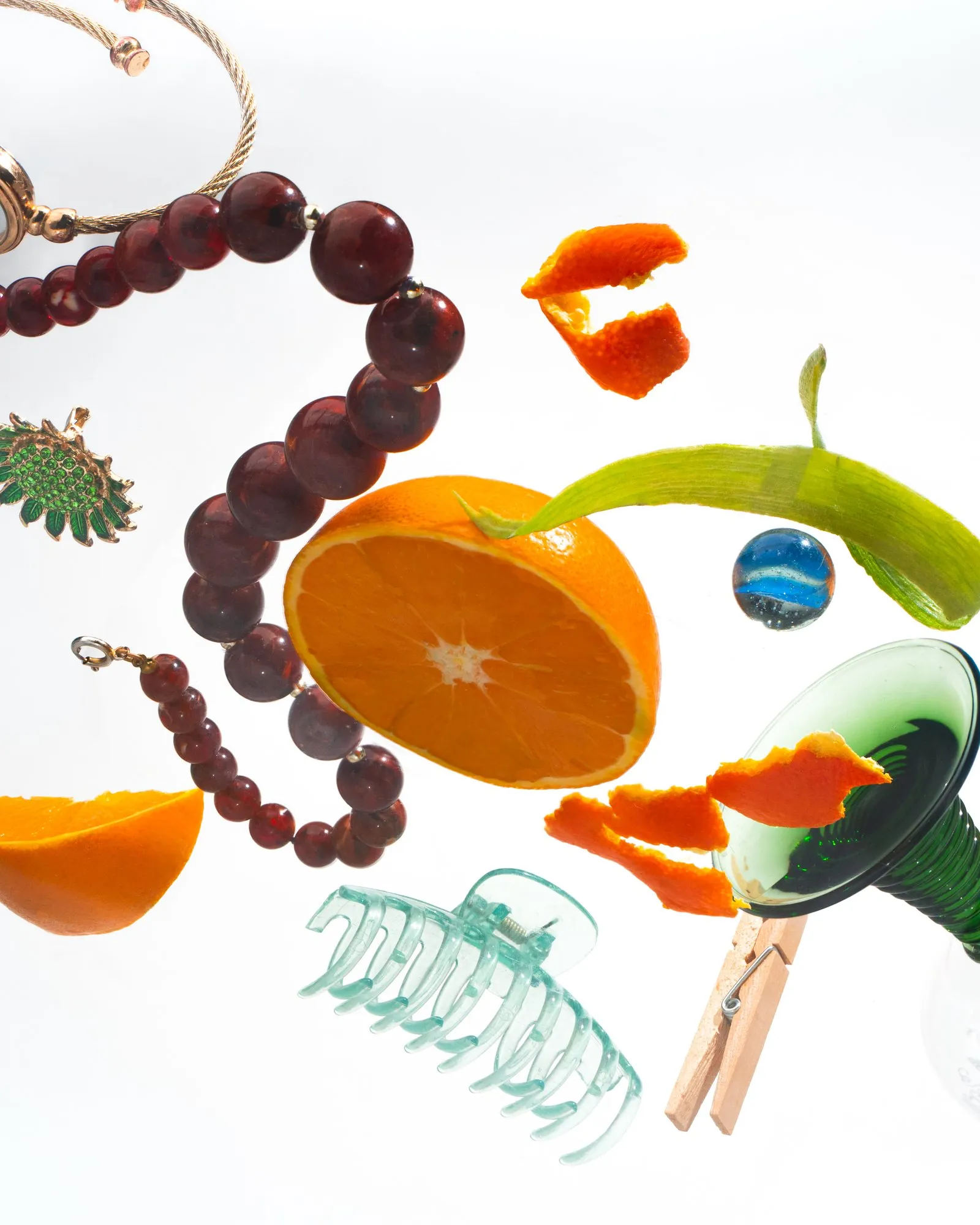 Orange halves, cherries, beads, a hair clip, and peel floating on white