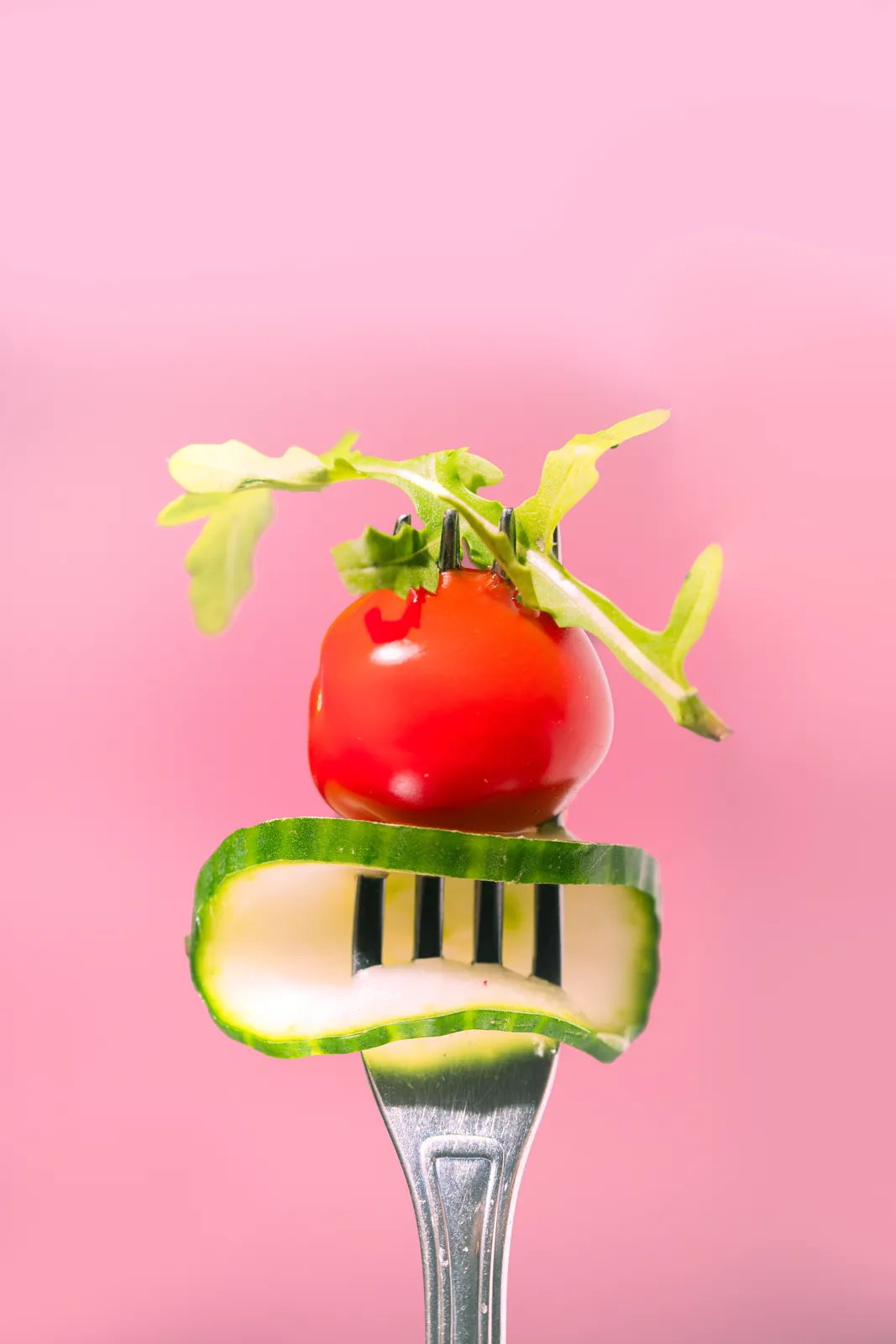 A tomato and cucumber stack speared on a fork on pink