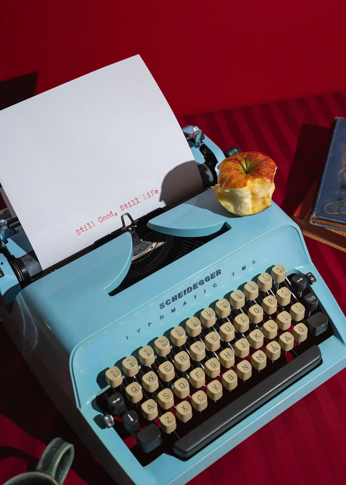 A turquoise typewriter typing Still Good, Still Life on red