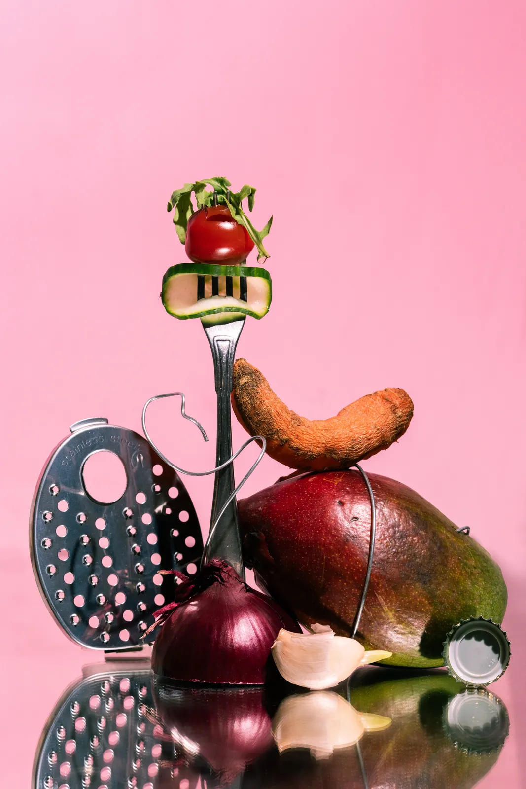 A fork, grater, sausage, and onion balanced on pink