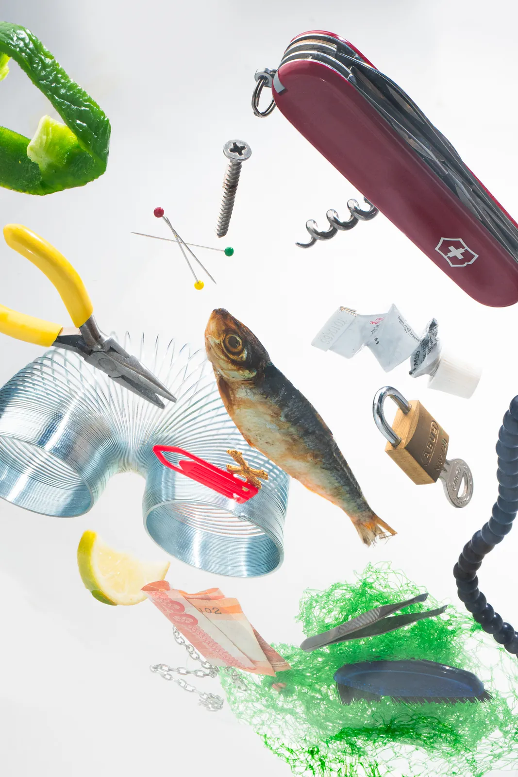 A fish, pocket knife, padlock, and pins floating on white