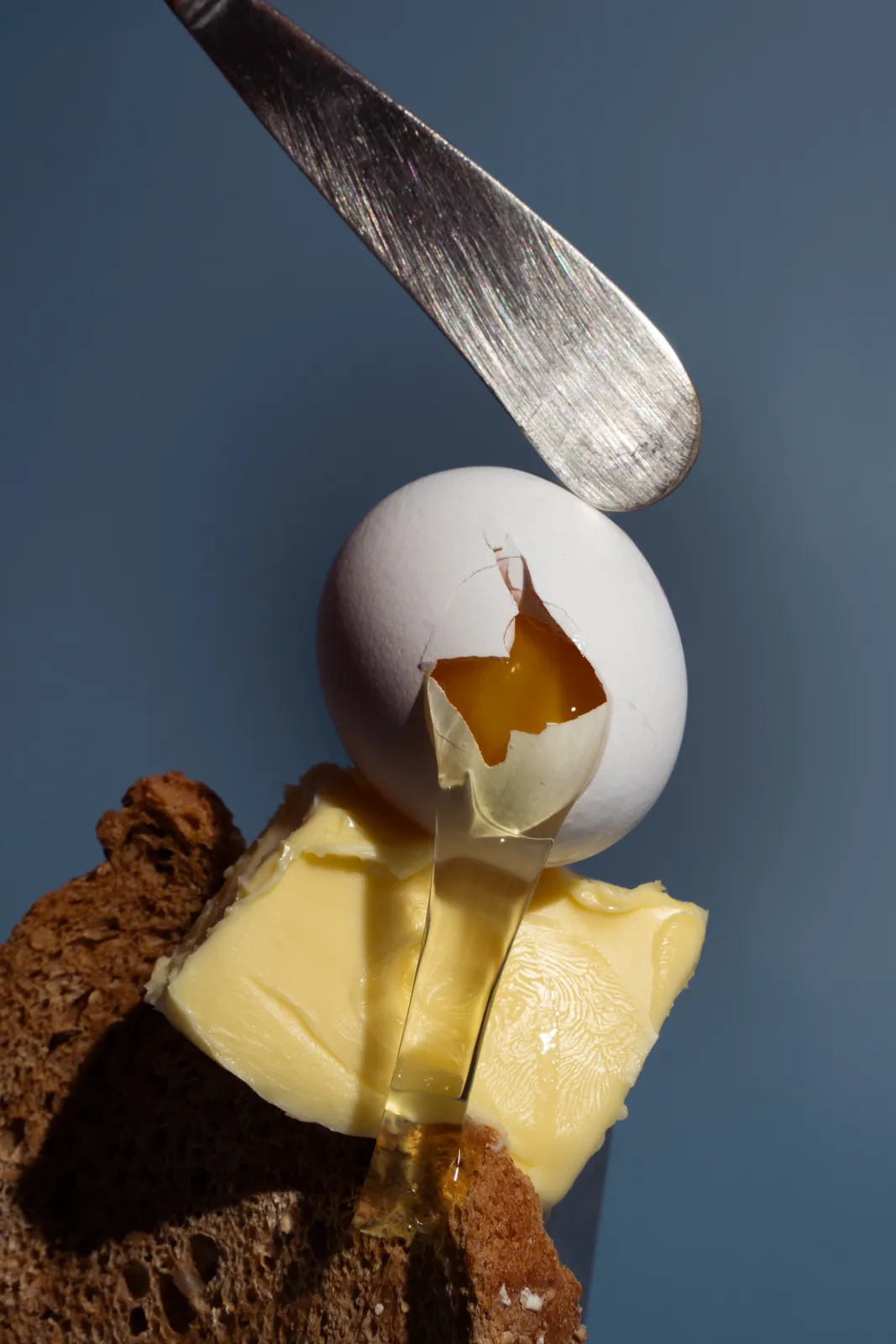 A knife hovering over an egg, butter and dark bread