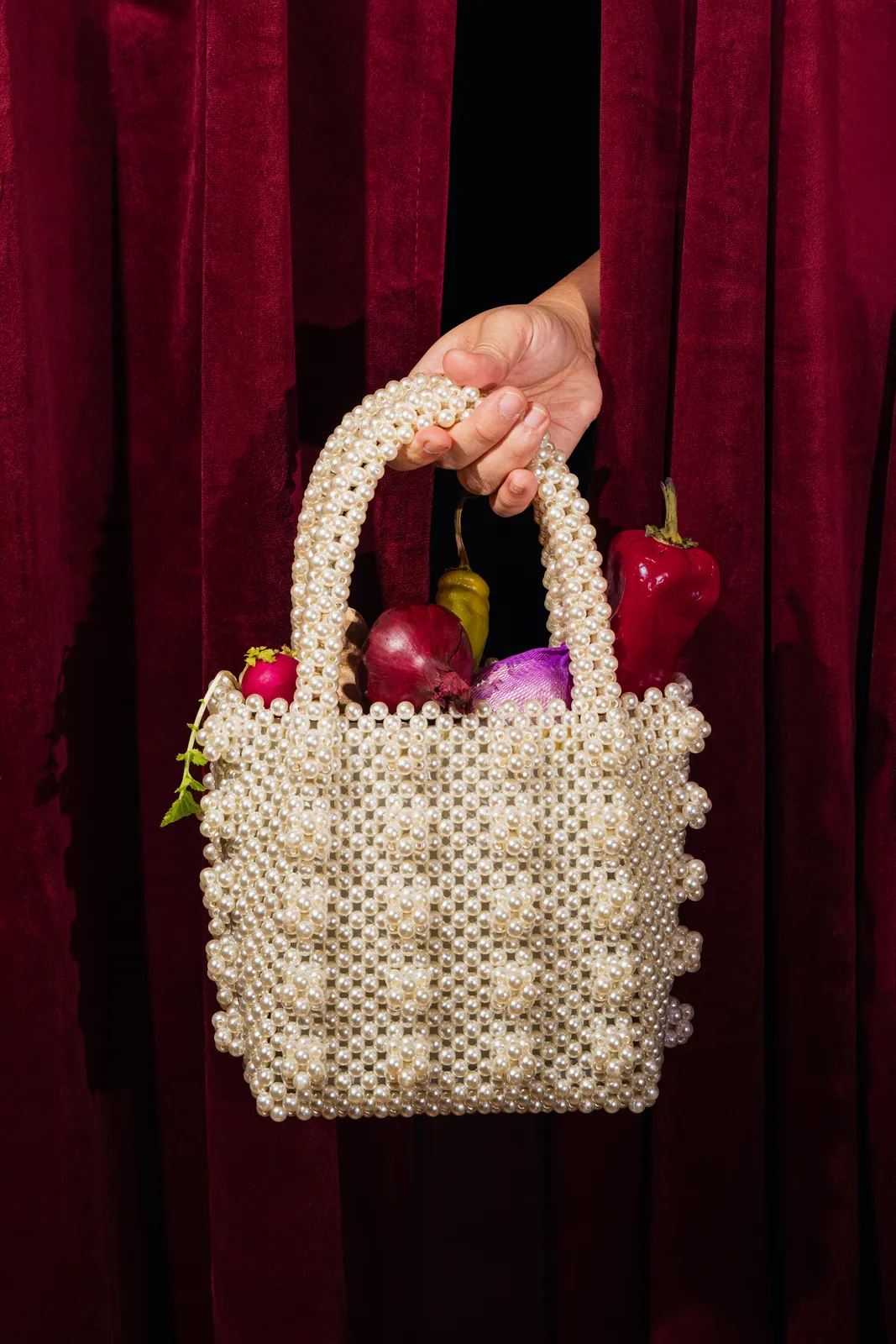 A hand holding a beaded bag of red onions