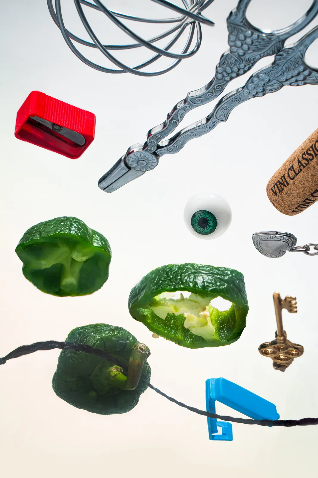Green peppers, a whisk, and a key floating on white