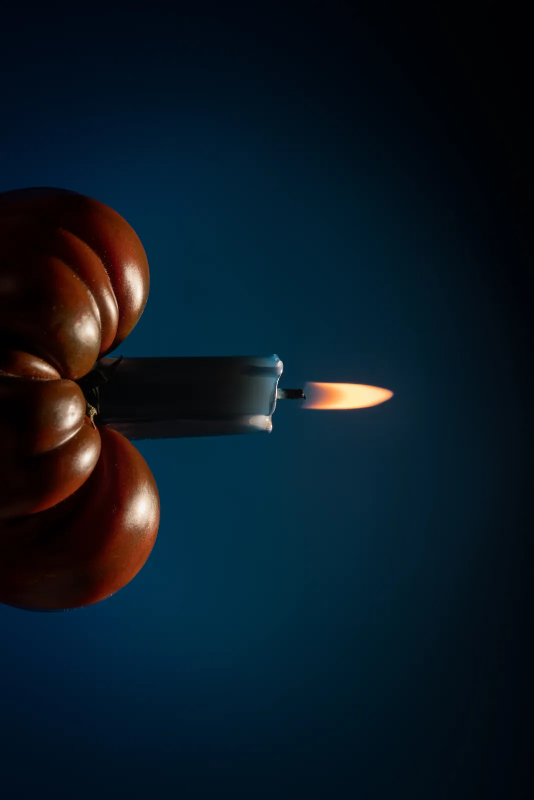 A lighter flame held up to a tomato in the dark