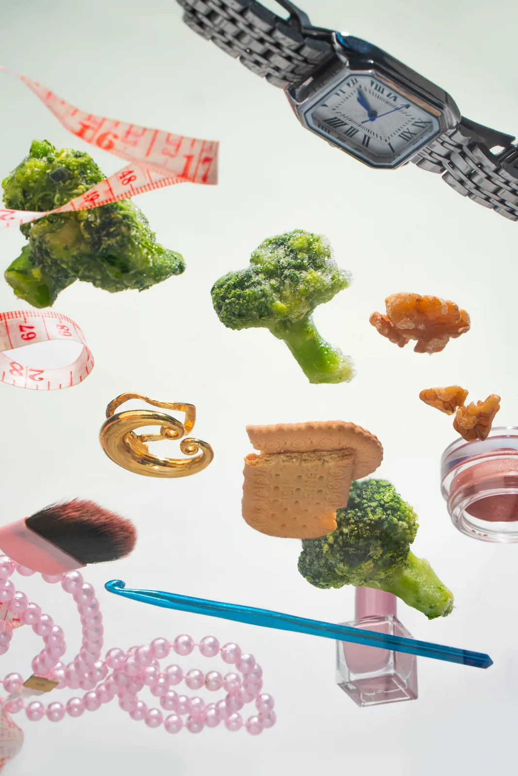 Broccoli, a watch, and pearls floating on white