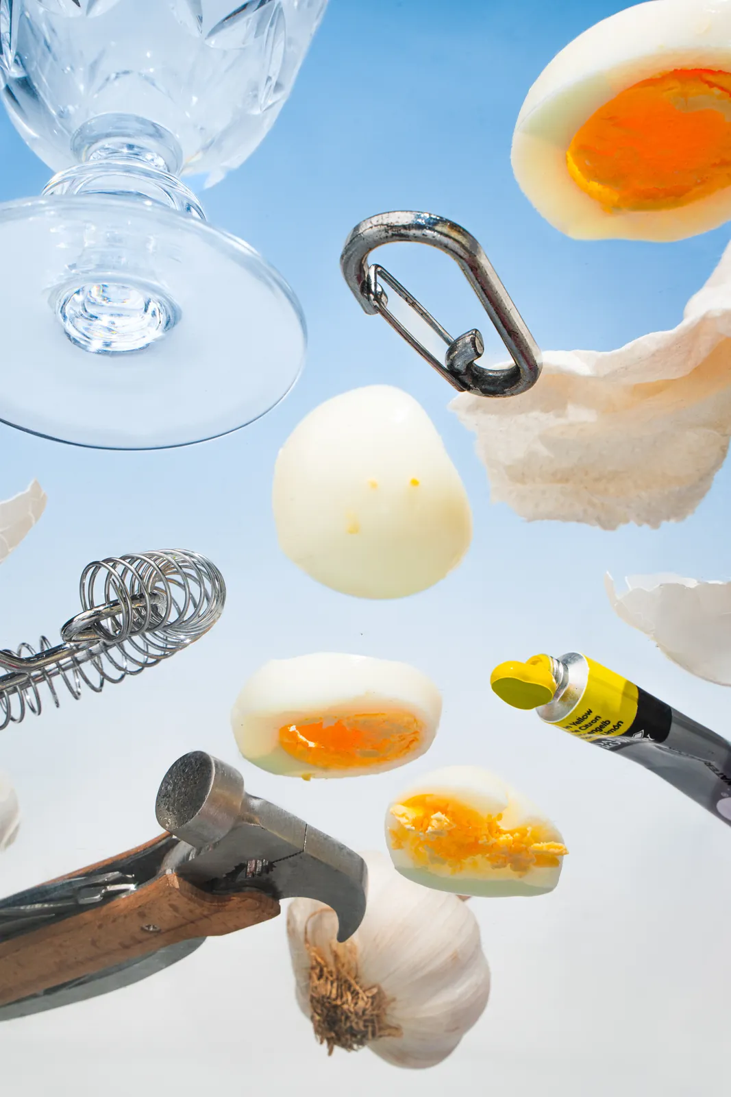Eggs, a hammer, and a carabiner floating on pale blue