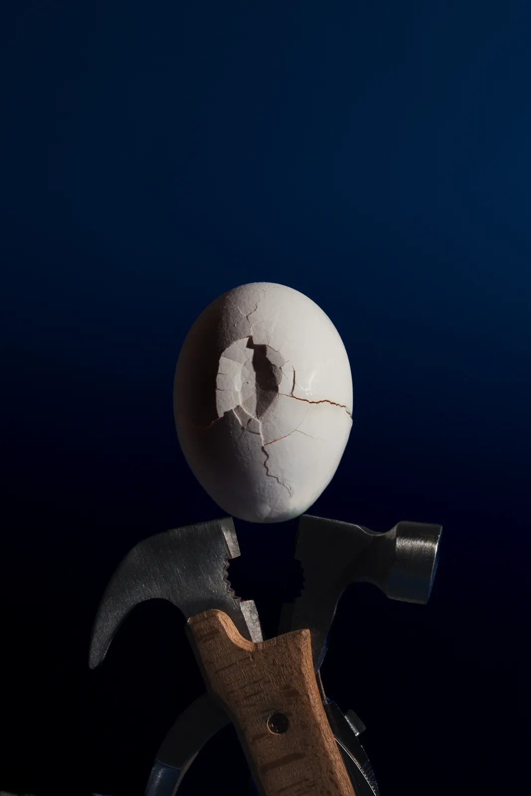 A cracked egg balanced on a hammer in the dark