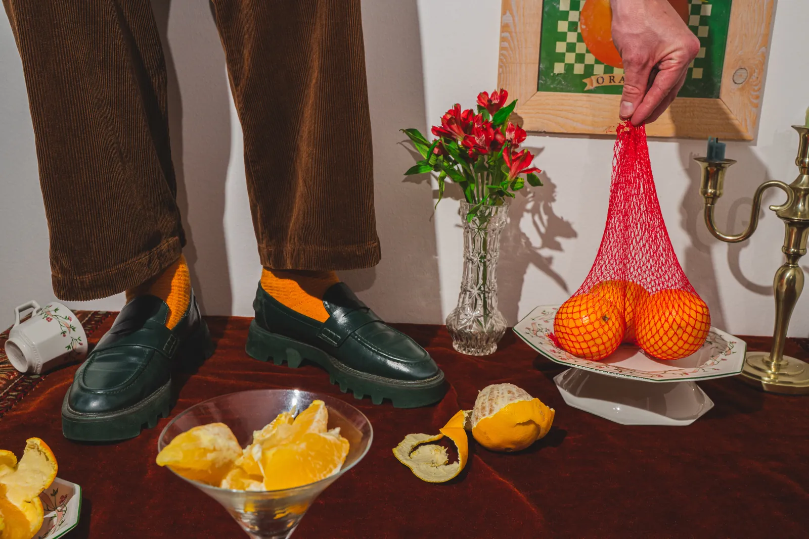 Legs in brown trousers beside oranges in a net bag
