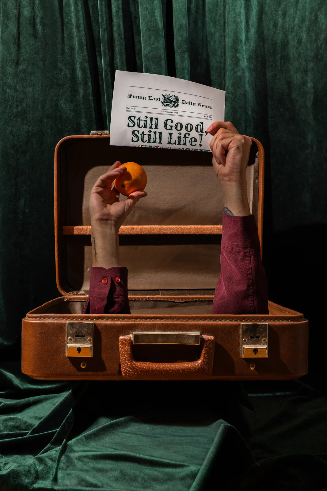 Hands holding a Still Good, Still Life newspaper out of a suitcase