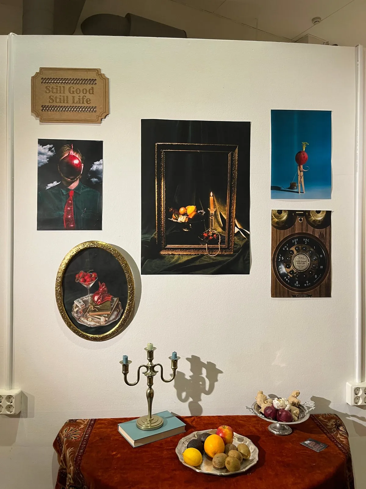 Framed still lifes above a styled table with candlesticks and fruit