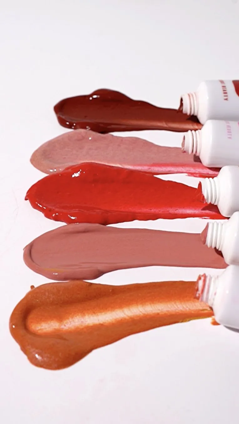 Five lip gloss tubes squeezing out swatches from berry to orange