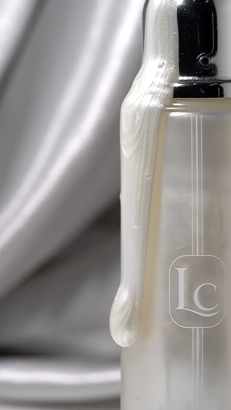 Pearly lotion dripping down a pump bottle on silver satin