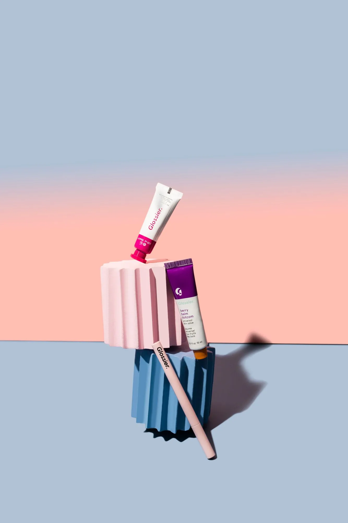 A Glossier tube balanced on a striped pedestal on lavender