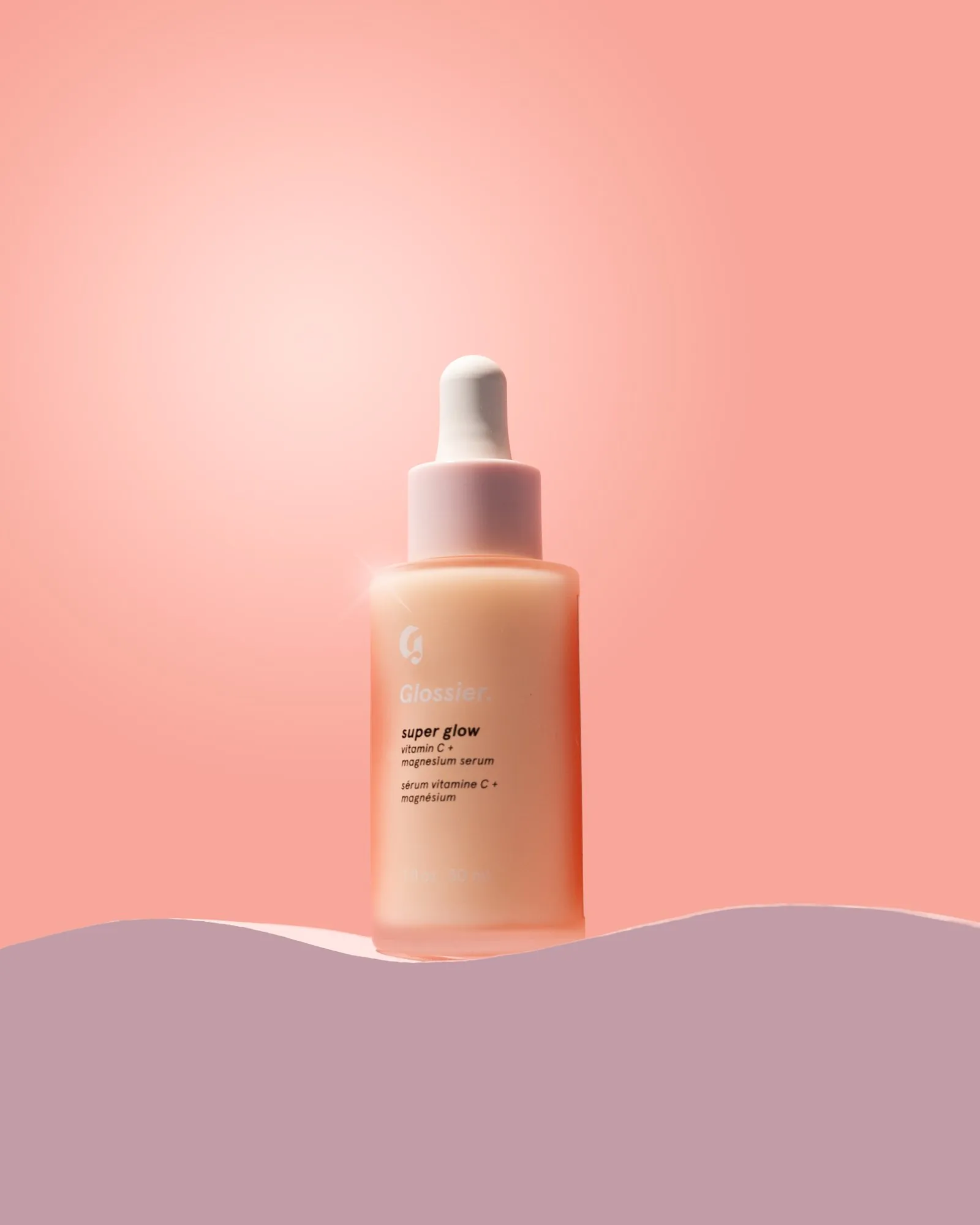 A Glossier serum bottle on a wavy pink set