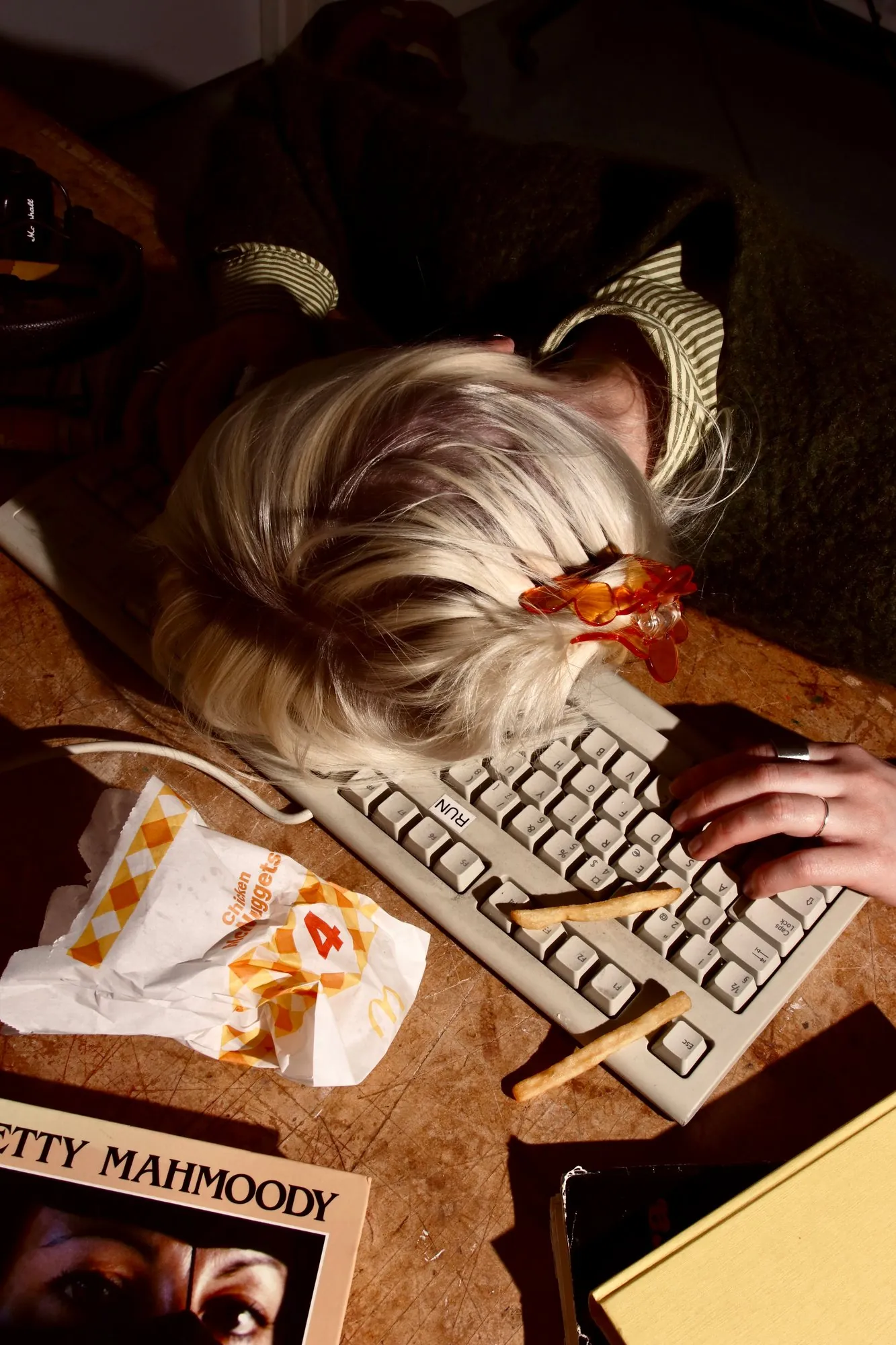A blonde head face-down on a keyboard beside a snack wrapper
