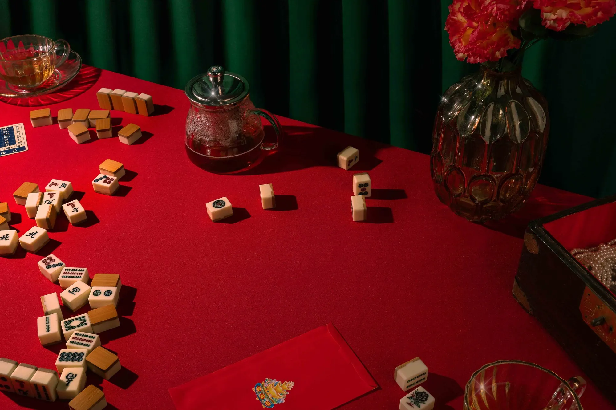 Mahjong tiles scattered on a red table with a green curtain