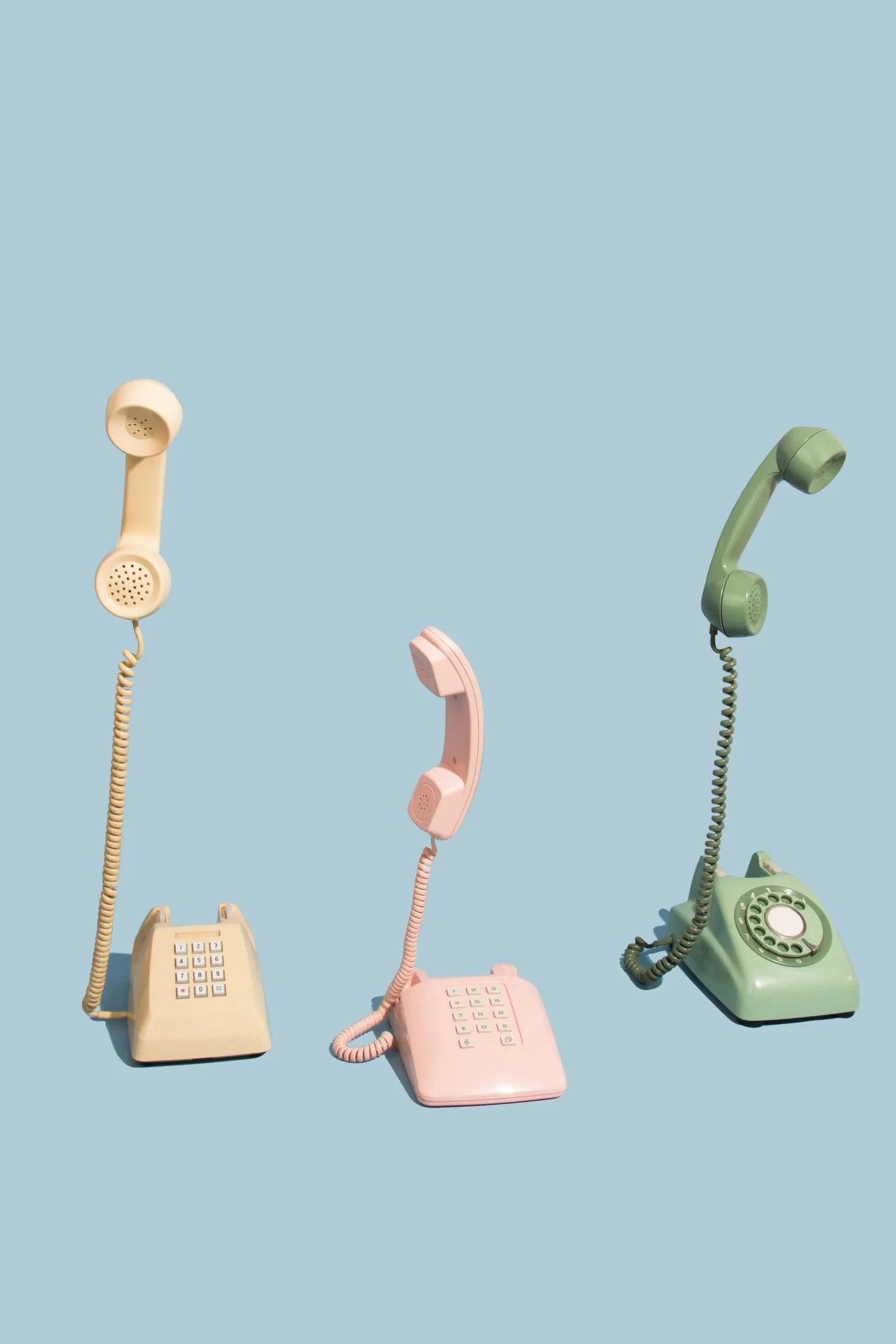 Three vintage telephones floating on pale blue